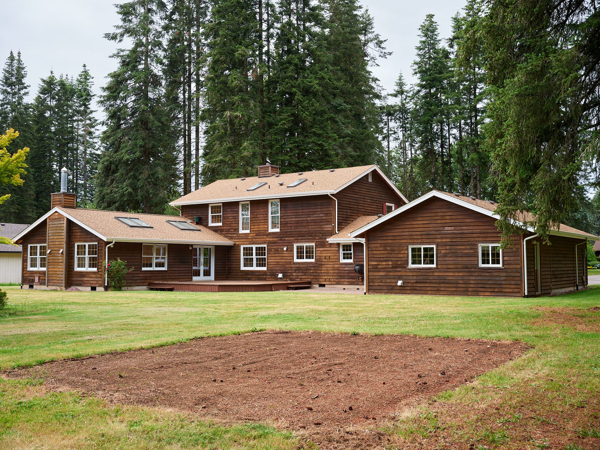 Rear elevation of the cedar home with its deck, backed by tall Douglas firs